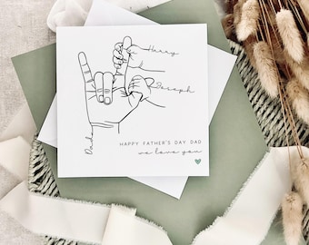 May include: A white card with a black line drawing of three hands holding each other. The text "Happy Father's Day Dad we love you" is written below the drawing. The names "Harry" and "Joseph" are written above the drawing.