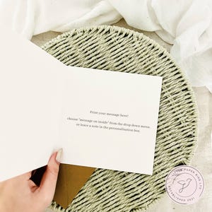 K&ouml;nnte beinhalten: Eine offene Gru&szlig;karte mit dem Text "Print your message here!". Die Karte wird &uuml;ber einem geflochtenen Platzset und einem braunen Umschlag gehalten. Das Logo von Little Paper Bird Ltd befindet sich in der unteren rechten Ecke. Das Innere der Karte ist leer.