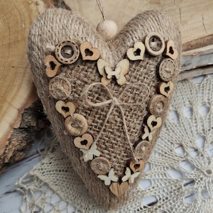Peut inclure: Un coussin en forme de cœur en toile de jute brune avec un nœud en ficelle brune et des boutons, des cœurs et des papillons en bois.