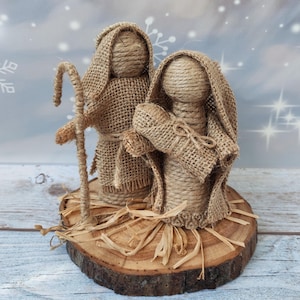 Könnte beinhalten: Eine rustikale Weihnachtskrippe aus Sackleinen und Schnur. Die Figuren von Maria, Josef und dem Jesuskind stehen auf einer Holzscheibe. Die Szene ist mit Stroh und Schnur dekoriert.