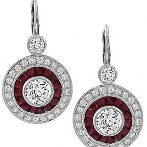 May include: A pair of silver drop earrings with a round design. Each earring features a large round clear stone surrounded by a ring of red stones and a halo of smaller clear stones. The earrings have a simple silver hook fastening.