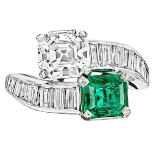 Puede incluir: Un anillo de platino con una gran piedra preciosa verde esmeralda y un diamante más pequeño de forma cuadrada. El anillo está engastado con diamantes de talla baguette.