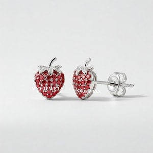 May include: A pair of silver earrings shaped like strawberries with red and white cubic zirconia stones.