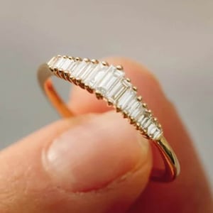 May include: A gold band ring with a row of baguette-cut diamonds set in a curved design.