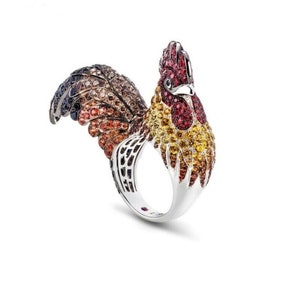 May include: A silver ring shaped like a rooster, with a red, orange, yellow, and brown jeweled design.