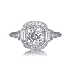 May include: A silver ring with a large, square-cut, clear gemstone at the center, surrounded by smaller, round gemstones. The ring has a vintage design with baguette-cut stones on each side of the center stone.