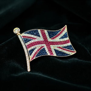 Op de afbeelding: Een broche van goudkleurig metaal in de vorm van de Union Jack-vlag, met rode, witte en blauwe kristallen.