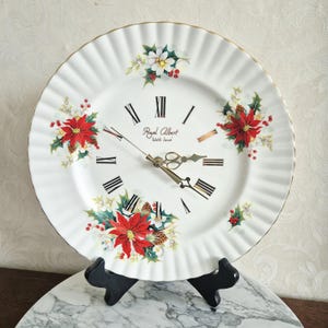Impresionante reloj de pared de Royal Albert Bone China, Inglaterra. Decorado con una flor de Pascua, una estrella roja de Navidad, flores blancas, hojas de acebo y un borde dorado.