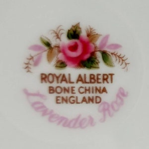 May include: A close-up of a Royal Albert bone china teacup with a lavender rose design. The text "Royal Albert Bone China England Lavender Rose" is printed in gold on the cup.