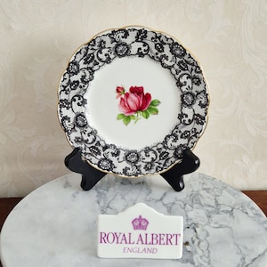 以下が含まれることがあります： 黒いレース模様と中央に赤いバラが描かれた、Royal Albert Englandの装飾用プレート。 金色の縁取りがあり、黒いスタンドに飾られています。クラシックなデザインです。