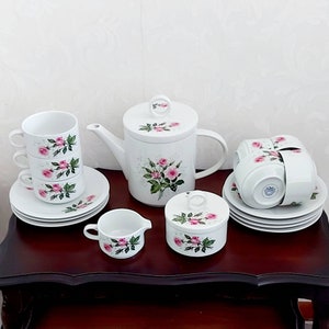 May include: A white tea set with a floral design featuring pink roses. The set includes a teapot, sugar bowl, creamer, and four cups and saucers.
