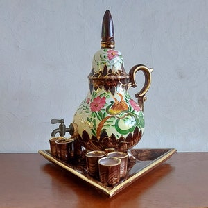 May include: A white ceramic teapot with a brown handle and floral design. The teapot has a spout with a small tap and is sitting on a wooden tray with four small ceramic cups.