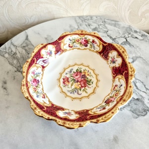 May include: A white porcelain bowl with a scalloped edge and a floral design. The bowl has a red and gold rim and a floral pattern in the centre.