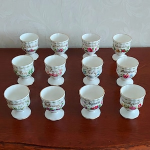 Peut inclure: Douze coquetiers en porcelaine blanche avec une bordure dorée, chacun décoré d'un mois différent de l'année et de motifs floraux.