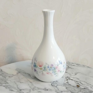 May include: A white ceramic vase with a floral pattern in shades of pink, blue, and green. The vase has a narrow neck and a rounded body.