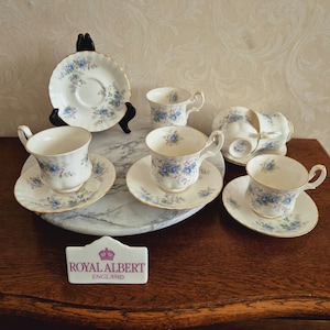 Könnte beinhalten: Ein Set aus sechs Royal Albert Teetassen und Untertassen im Muster Old Country Roses. Die Tassen und Untertassen sind weiß mit einem zarten Blumendesign in Blautönen und Rosa. Das Set wird auf einer Marmorfläche mit einem Royal Albert Logo präsentiert.