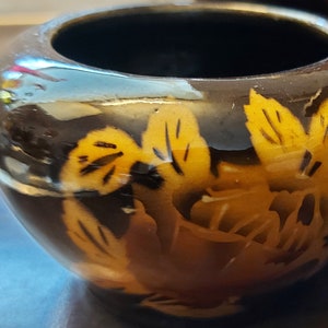 May include: A small, round, dark brown decorative bowl with a glossy finish. The bowl features a floral design in shades of yellow and orange. The interior of the bowl is black.
