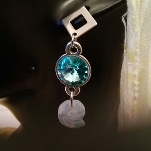Puede incluir: Pendientes de plata con un cristal azul turquesa y un encanto blanco en espiral.