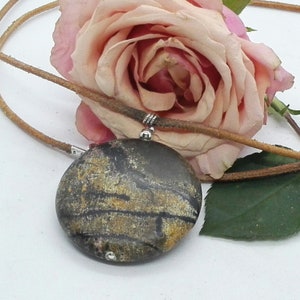 May include: A brown and gold stone pendant with a leather cord necklace. The stone has a striped pattern.