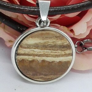 Peut inclure: Un pendentif rond en argent avec une pierre rayée brune et blanche. Le pendentif est sur un cordon en cuir brun.