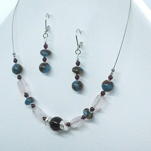 May include: A silver necklace and earrings set with blue, pink, and maroon glass beads. The necklace features a larger, dark maroon bead in the center.