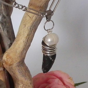 May include: A black and silver pendant necklace featuring a black stone wrapped in silver wire and topped with a white pearl.
