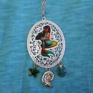 May include: Silver necklace with a mermaid charm, a seashell charm, and two starfish charms. The mermaid charm is a colorful illustration of a mermaid with long black hair and a green tail.