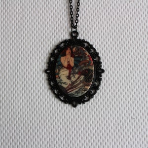May include: A black necklace with a round pendant featuring a vintage illustration of a woman in a white dress. The pendant has a black filigree design around the edge.