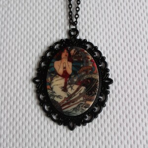 May include: A black chain necklace with a cameo pendant featuring a vintage illustration of a woman in a white dress with red accents. The cameo is surrounded by a black filigree frame.