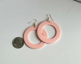 Op de afbeelding: Een paar roze creolen met een gouden haaksluiting. De oorbellen zijn ongeveer zo groot als een muntstuk van 25 cent.
