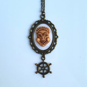 May include: A bronze necklace with a cameo featuring a smiling face and a bronze ship's wheel pendant.