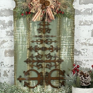 May include: A rustic wooden fence with a Christmas wreath and a metal tree made of hinges. The wreath is decorated with red berries, a plaid bow, and a burlap bow. The fence is painted a light blue-green color and has a distressed finish.