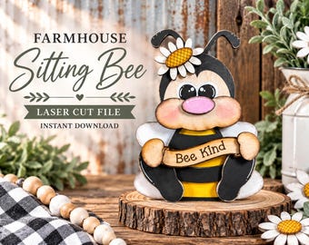 Puede incluir: Una figura de abeja de madera cortada con láser con rayas negras y amarillas, una nariz rosa y una margarita blanca en la cabeza. La abeja sostiene una pancarta con el texto Bee Kind. El texto Farmhouse Sitting Bee Laser Cut File es visible.
