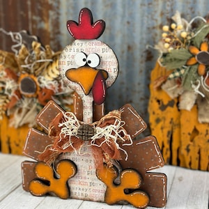 Pu&ograve; includere: Una decorazione in legno a forma di tacchino con cresta rossa, grandi occhi bianchi e becco arancione. Il corpo presenta una stampa con testo che include apple pie e cranberry. &Egrave; decorato con un fiocco in tessuto marrone e un bottone in legno.