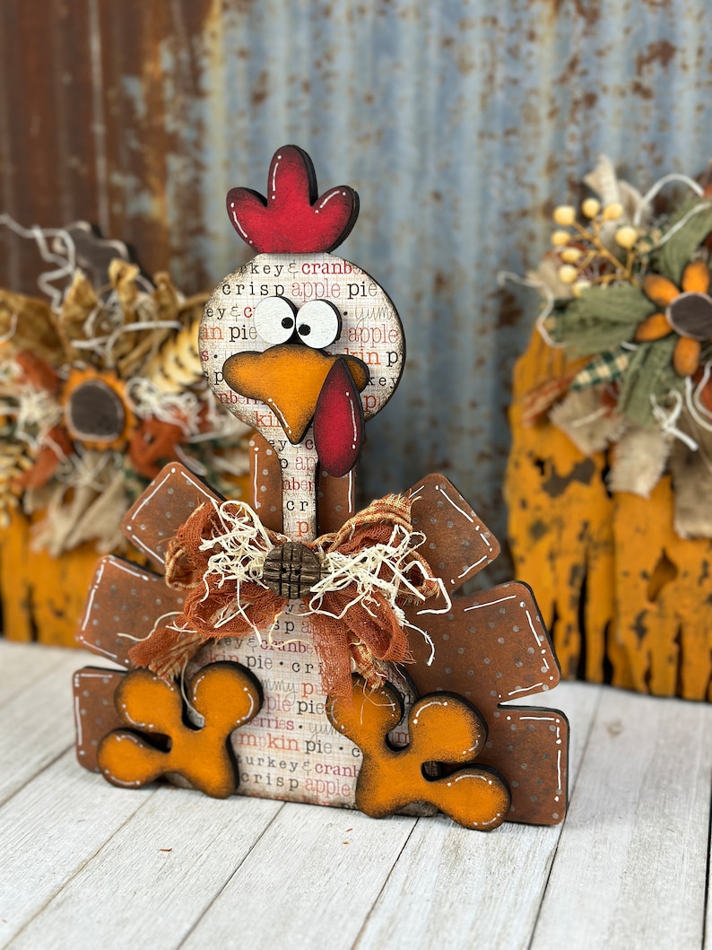 Pu&ograve; includere: Una decorazione in legno a forma di tacchino con cresta rossa, grandi occhi bianchi e becco arancione. Il corpo presenta una stampa con testo che include apple pie e cranberry. &Egrave; decorato con un fiocco in tessuto marrone e un bottone in legno.