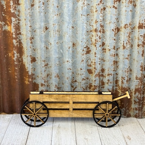 May include: A wooden miniature wagon with black wheels and a brown wooden bed. The wagon is sitting on a white wooden surface.