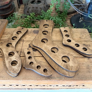 Può includere: Una collezione di forme per calzini in legno di varie dimensioni. Ogni forma è tagliata a forma di calzino con più fori circolari. Il legno ha una macchia scura e le forme sono disposte su una superficie di legno.