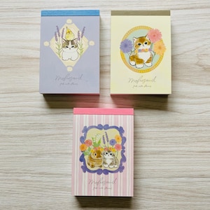 May include: Three notebooks with illustrated covers. One features a cat and bird with lavender, another a cat with flowers, and the third has two animals with flowers. The notebooks have the text "Mofusand" and "pink cute flowers".