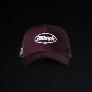 May include: A maroon trucker hat with a white embroidered logo that reads "200mph CLUB". The hat has a mesh back and a curved brim. The hat is set against a black background.