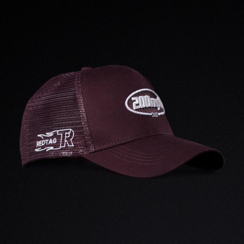 May include: A burgundy baseball cap with a mesh back and a curved brim. The cap features white embroidered text on the front and side, including the words "200m" and "REDTAG". The hat is designed for casual wear.