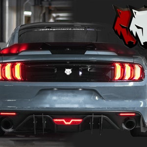 May include: A gray Ford Mustang with red taillights and a black rear diffuser. The car has a wolf emblem on the back. The text "redtagmiami.com" is visible on the rear window.