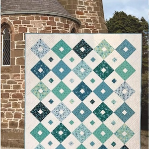 May include: A large, quilted blanket with a repeating diamond pattern in shades of teal, blue, and white. The quilt is displayed outdoors, with a stone building in the background. The quilt's design features a central square within each diamond.