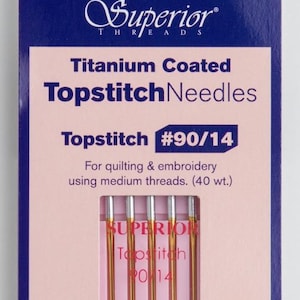 May include: A package of six titanium coated topstitch needles in size 90/14, for quilting and embroidery using medium weight thread. The package is pink and blue with the text "Superior Threads" and "Topstitch Needles" printed on it.