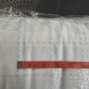Könnte beinhalten: Ein rotes Maßband mit schwarzen Markierungen liegt auf einer weißen Oberfläche mit einem Gittermuster. Das Band zeigt "1 Zoll" an und hat Markierungen bis zu 6 Zoll.