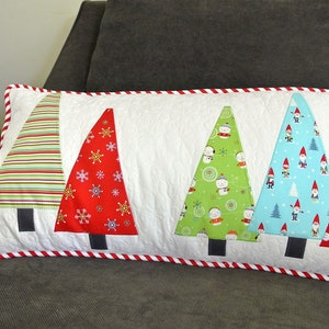 May include: A white rectangular pillow with a red and white striped border. The pillow is decorated with five appliqued Christmas trees in various patterns, including stripes, snowflakes, snowmen, gnomes, and polka dots.