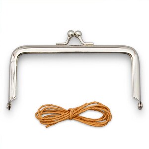 May include: A silver-colored metal purse frame with a kiss-lock clasp and a matching brown cord. The frame is rectangular with rounded corners and small ball accents on the clasp. The cord is bundled in a neat coil.