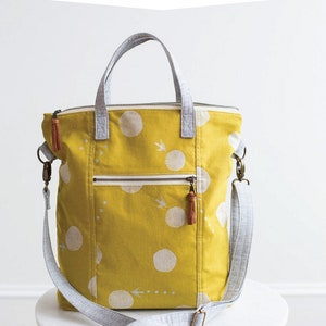 May include: A yellow tote bag with a white polka dot pattern and a zip top. The bag has a gray shoulder strap and handles. The text "REDWOOD TOTE" is at the top of the image.