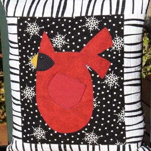 May include: A black and white striped pillow with a red cardinal applique. The cardinal is surrounded by white snowflakes on a black background with white polka dots.