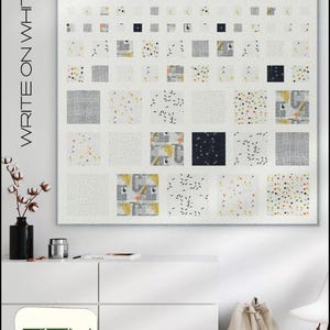 May include: A large, square quilt with a white background and a grid pattern of various square patches. The patches feature gray, yellow, and black accents. The text "WRITE ON WHITE" is on the left side of the quilt. The quilt is displayed above a white cabinet.
