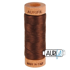 May include: A spool of brown Aurifil thread. The thread is tightly wound around a wooden core. The top of the spool has the Aurifil logo and the bottom reads "MADE IN ITALY". The thread is a rich, dark brown color.